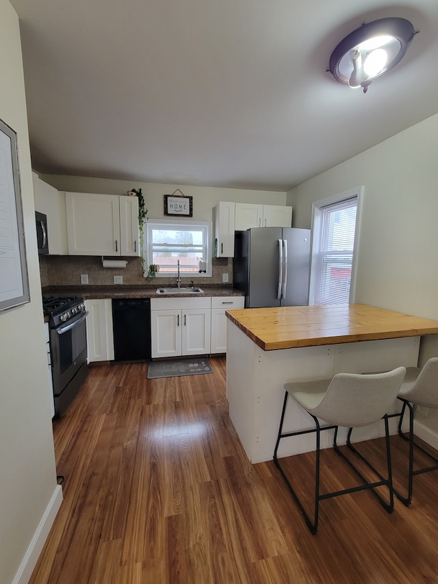 kitchen with black appliances, butcher block countertops, a sink, and white cabinetry