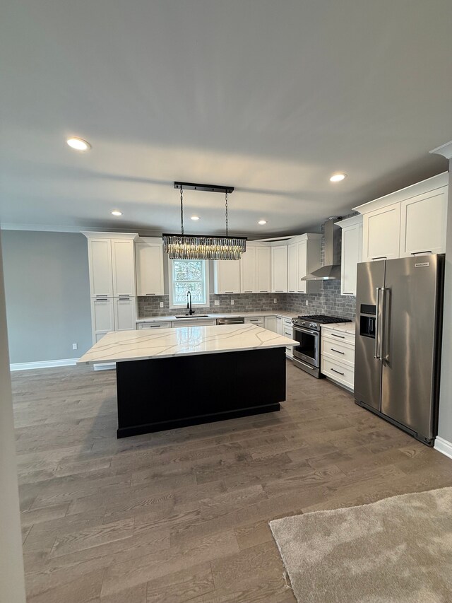 kitchen featuring wall chimney range hood, a sink, decorative backsplash, appliances with stainless steel finishes, and a kitchen island