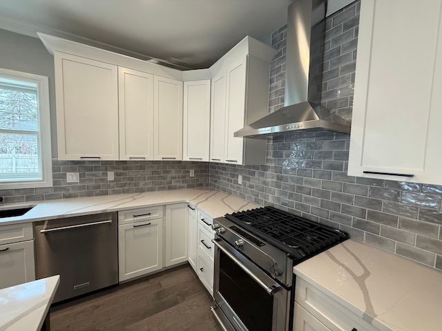 kitchen with light stone countertops, wall chimney exhaust hood, appliances with stainless steel finishes, and decorative backsplash