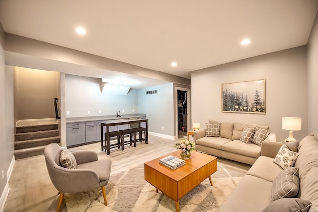 living area with stairway, wet bar, visible vents, baseboards, and light wood-style flooring