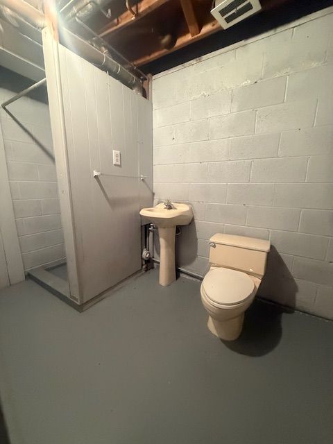 full bath with a shower, concrete block wall, toilet, finished concrete floors, and a sink