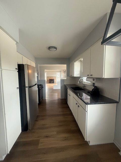 kitchen featuring dark wood finished floors, dark countertops, freestanding refrigerator, white cabinetry, and a sink