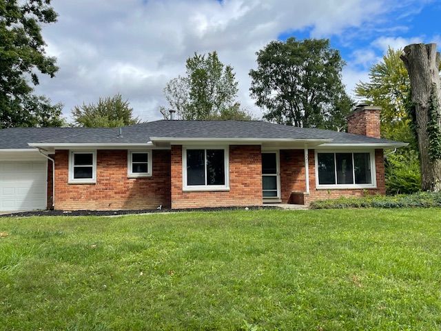 ranch-style home with brick siding, a chimney, a shingled roof, an attached garage, and a front lawn