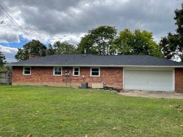 back of property with an attached garage, brick siding, a chimney, and a yard