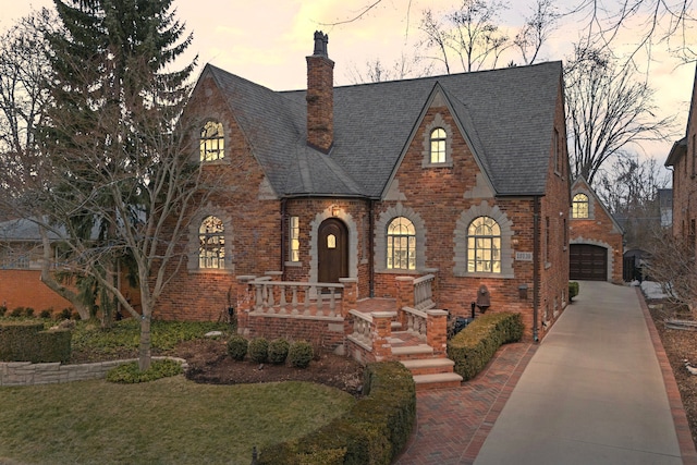 tudor-style house with brick siding, roof with shingles, a chimney, a porch, and a front lawn