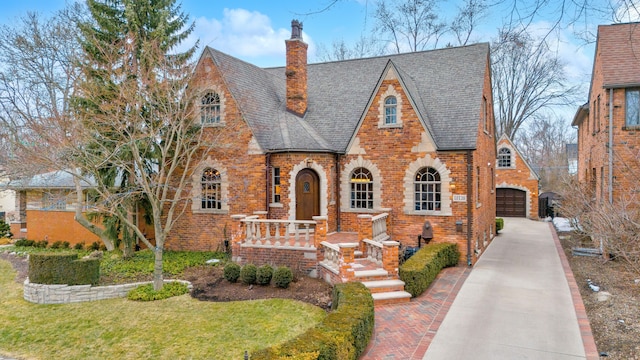 tudor home with brick siding, a chimney, a shingled roof, a garage, and a front lawn