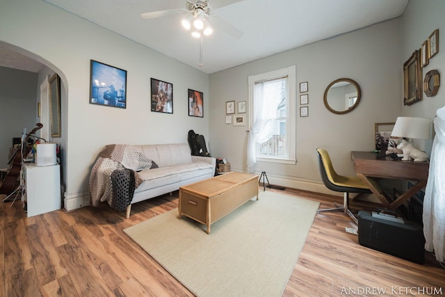 living room featuring arched walkways, ceiling fan, light wood-type flooring, and baseboards