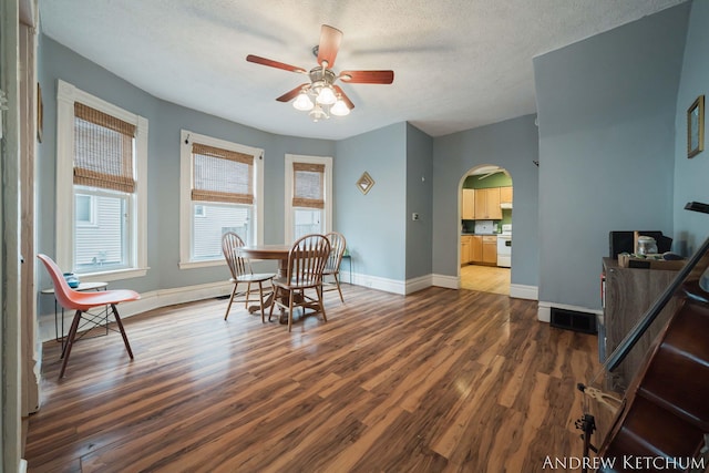 dining space with baseboards, arched walkways, a ceiling fan, dark wood finished floors, and a textured ceiling