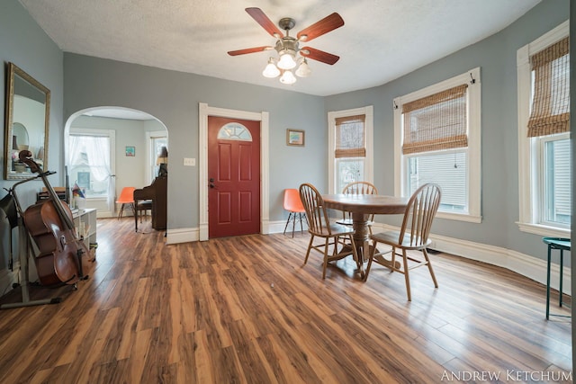 dining room featuring arched walkways, ceiling fan, baseboards, and wood finished floors