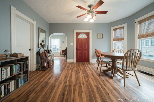 dining space featuring arched walkways, a healthy amount of sunlight, baseboards, and wood finished floors