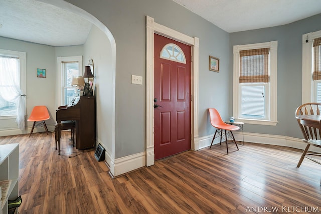 foyer entrance featuring baseboards, arched walkways, dark wood finished floors, and a textured ceiling