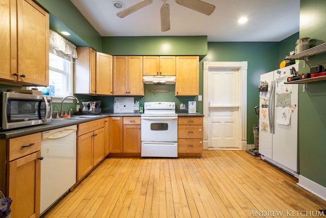 kitchen with light wood finished floors, dark countertops, a sink, white appliances, and under cabinet range hood