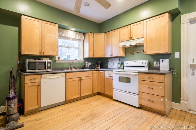 kitchen with light brown cabinets, under cabinet range hood, white appliances, a sink, and dark countertops