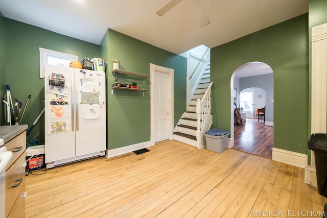 kitchen with arched walkways, a ceiling fan, baseboards, freestanding refrigerator, and hardwood / wood-style floors