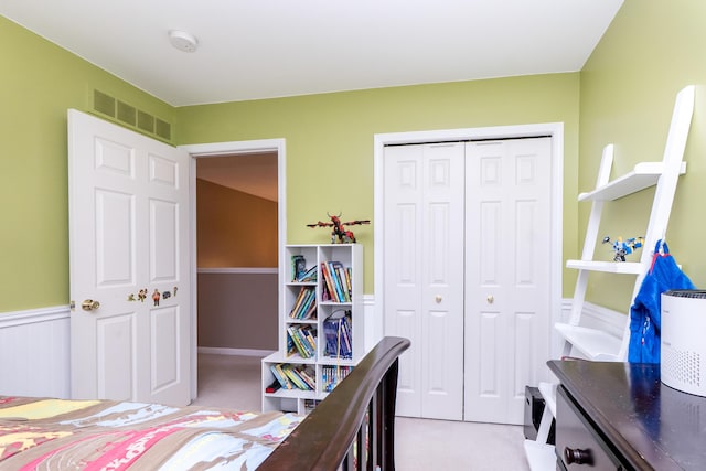 bedroom featuring light carpet, a closet, wainscoting, and visible vents