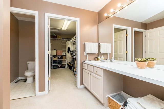 bathroom with toilet, baseboards, a walk in closet, and vanity