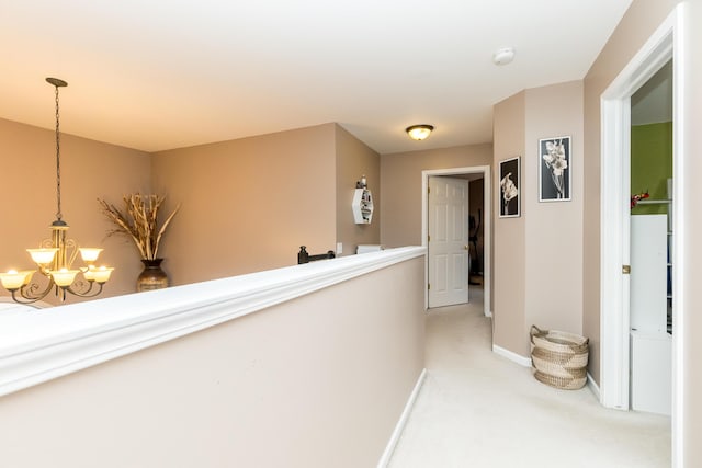 hall with light carpet, baseboards, and an inviting chandelier