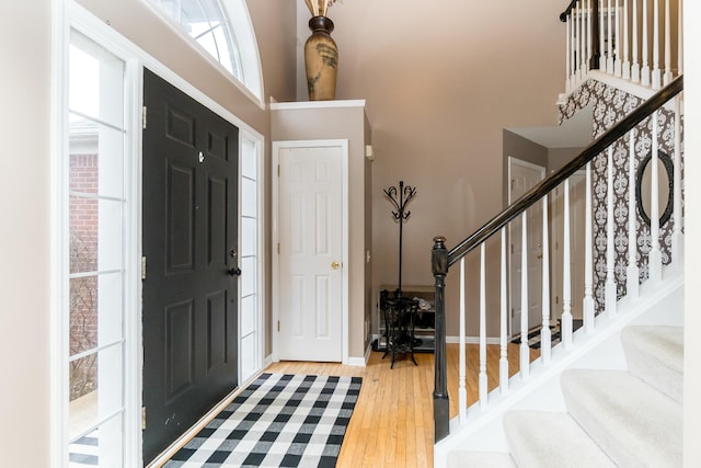 entryway featuring a towering ceiling, stairs, baseboards, and wood finished floors