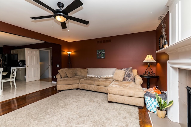 living area featuring ceiling fan, light wood-type flooring, a fireplace, and visible vents