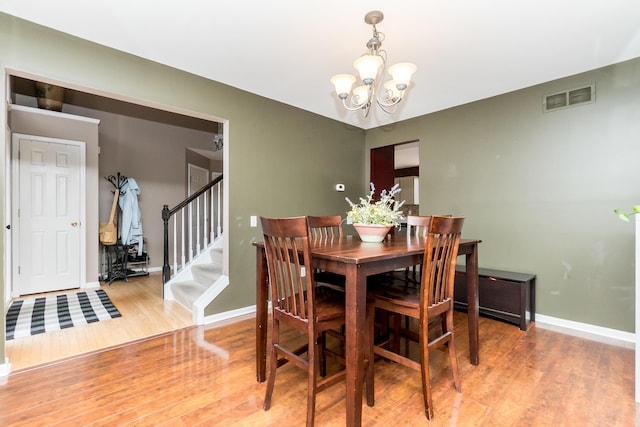 dining room with visible vents, wood finished floors, a chandelier, baseboards, and stairs