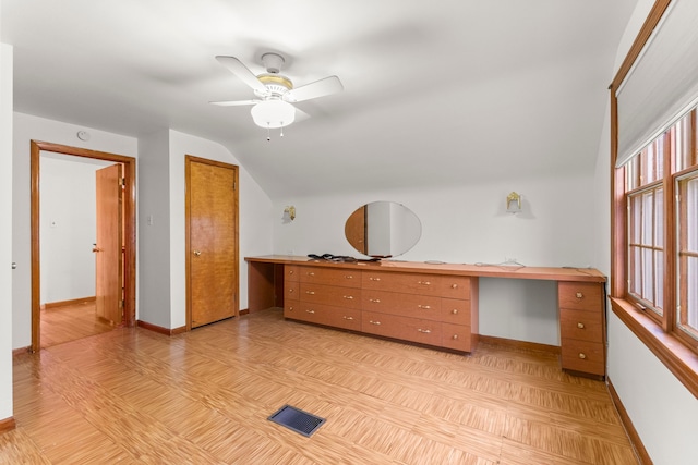 unfurnished office with built in desk, visible vents, vaulted ceiling, ceiling fan, and baseboards