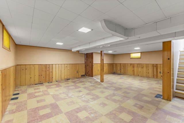 basement with light floors, stairs, wood walls, and wainscoting