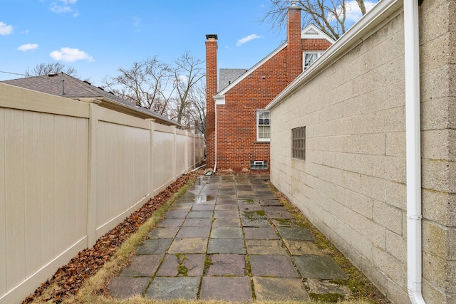 view of side of property featuring brick siding, fence, and a patio