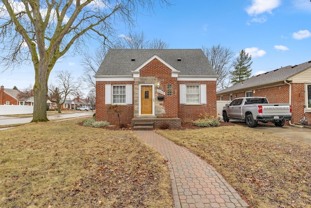 bungalow-style home featuring brick siding, a shingled roof, and a front yard