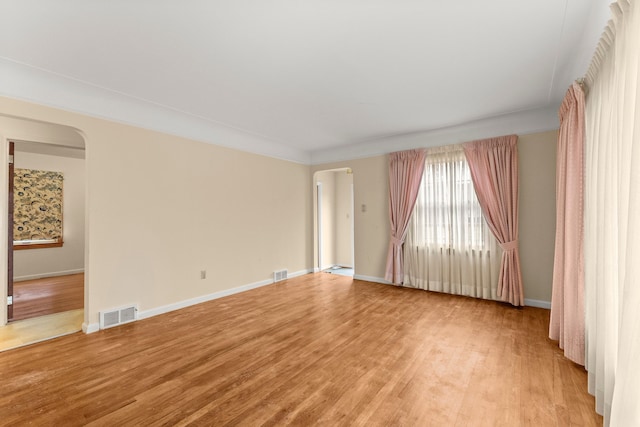 spare room with light wood-style floors, visible vents, arched walkways, and baseboards