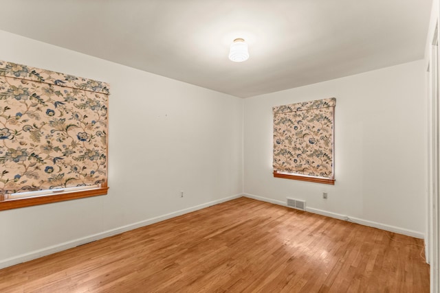 empty room with wood finished floors, visible vents, and baseboards