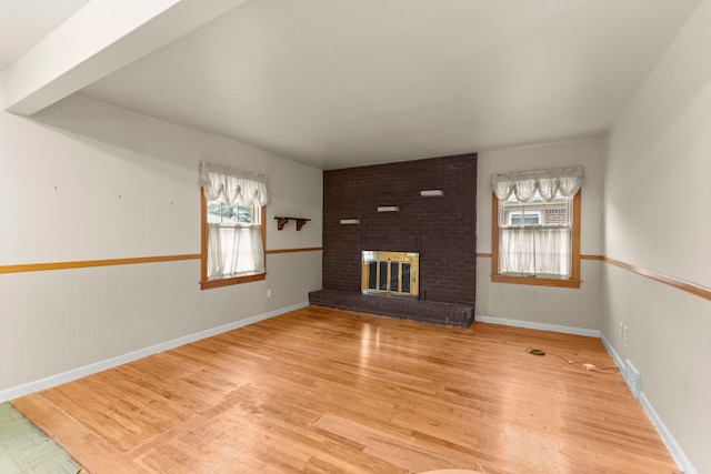 unfurnished living room featuring plenty of natural light, a wainscoted wall, a fireplace, and light wood-style floors