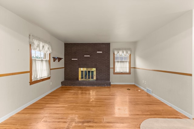 unfurnished living room featuring plenty of natural light, a fireplace, wood finished floors, and visible vents