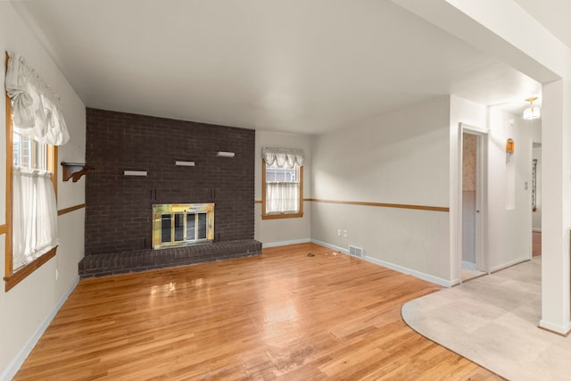 unfurnished living room with visible vents, a fireplace, baseboards, and wood finished floors