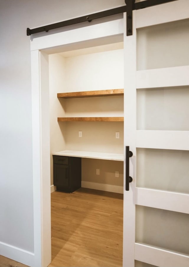 unfurnished office with baseboards, a barn door, built in desk, and light wood-style floors