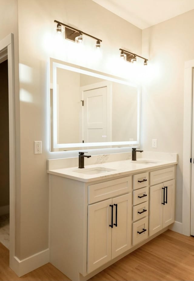 bathroom with double vanity, a sink, baseboards, and wood finished floors