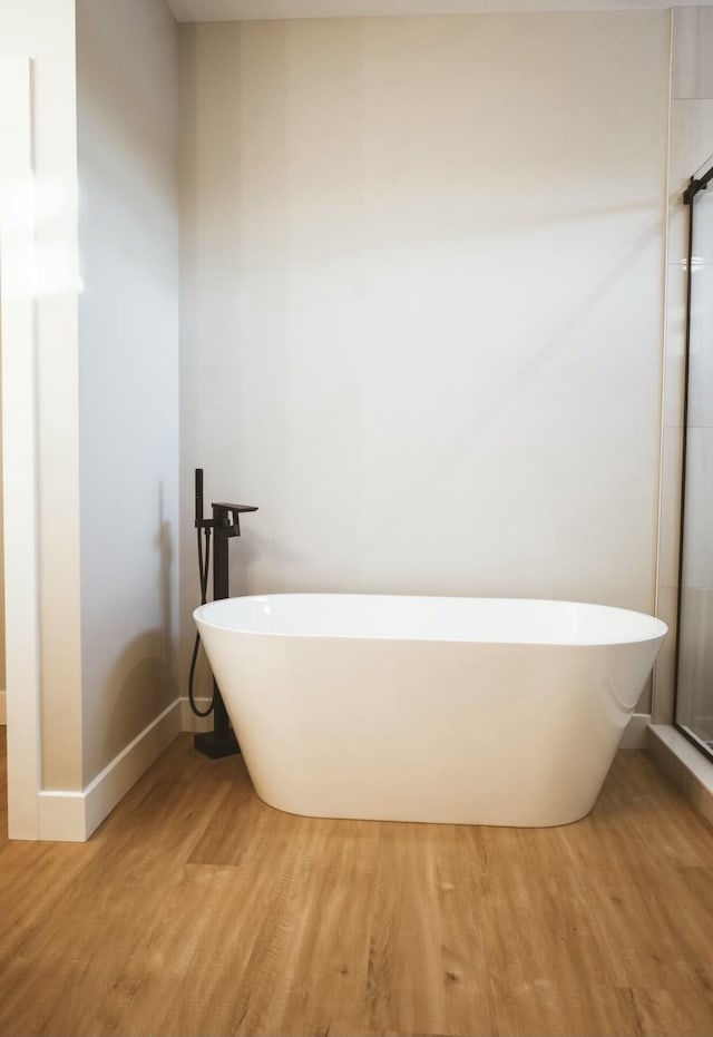 bathroom featuring a freestanding tub, baseboards, and wood finished floors