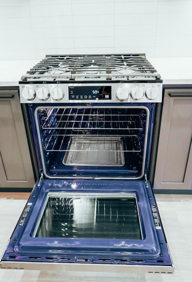 details featuring stainless steel gas range, gray cabinetry, and decorative backsplash