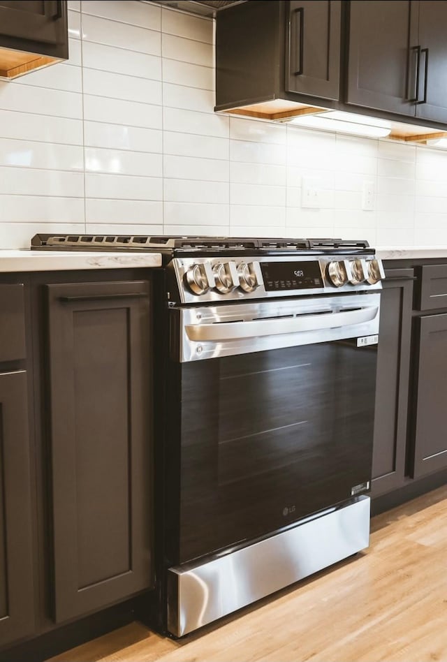 kitchen with light countertops, decorative backsplash, stainless steel range with gas stovetop, dark brown cabinets, and light wood-type flooring