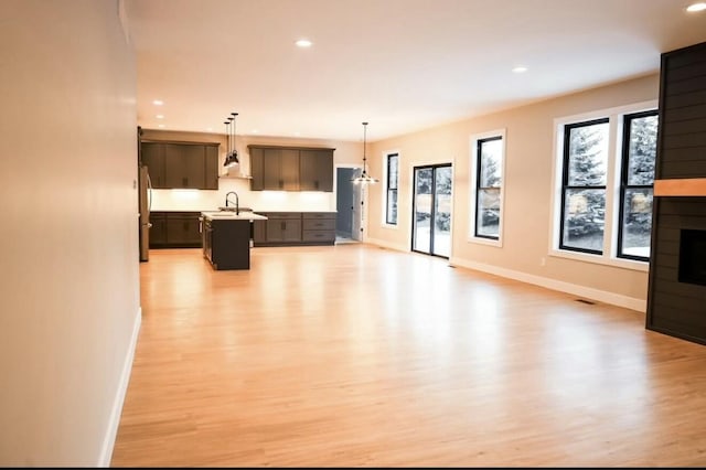 kitchen featuring an island with sink, open floor plan, freestanding refrigerator, light countertops, and a sink