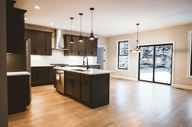 kitchen featuring a sink, light countertops, stainless steel dishwasher, wall chimney exhaust hood, and light wood finished floors