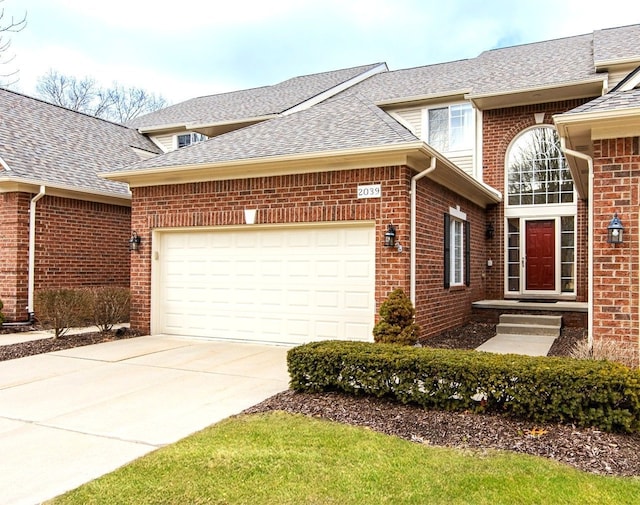 traditional home with concrete driveway, an attached garage, brick siding, and roof with shingles