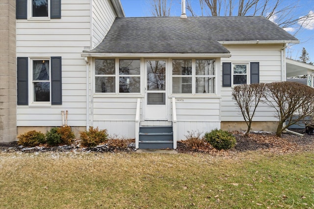 view of front of house with a shingled roof, a front yard, a sunroom, and entry steps