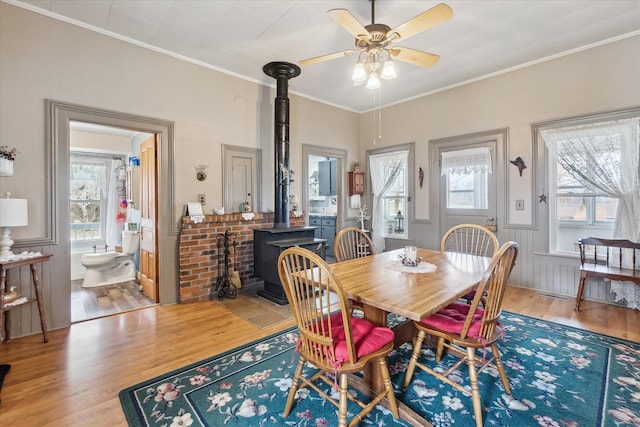 dining area with wainscoting, ceiling fan, wood finished floors, a wood stove, and crown molding