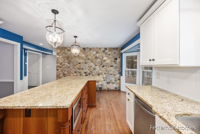 kitchen with white cabinets, light stone counters, decorative light fixtures, stainless steel appliances, and light wood-type flooring