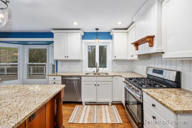 kitchen featuring a sink, light stone countertops, stainless steel appliances, white cabinetry, and backsplash