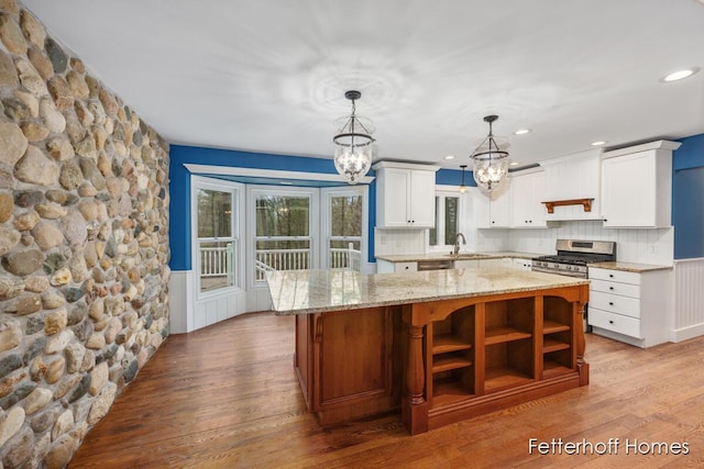 kitchen with a wainscoted wall, light wood-style flooring, a center island, a chandelier, and a sink