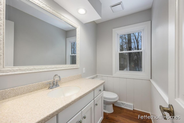 half bath with toilet, wainscoting, wood finished floors, and visible vents