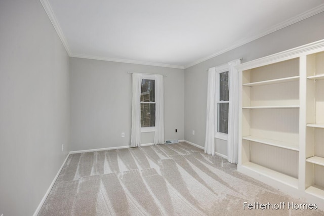 carpeted spare room featuring ornamental molding, built in shelves, visible vents, and baseboards