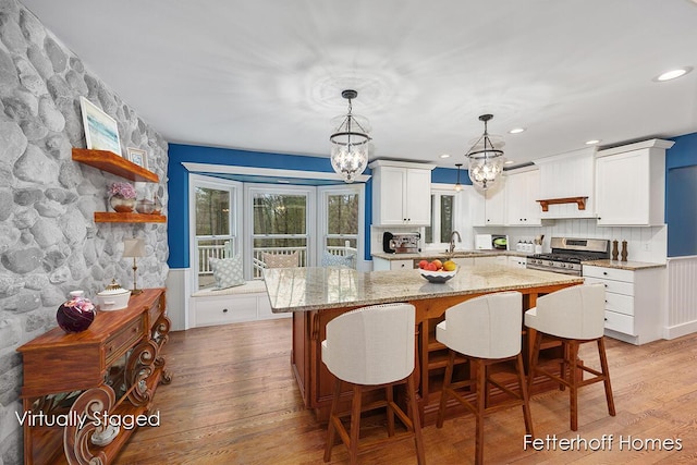 kitchen featuring light wood-type flooring, a center island, stainless steel range with gas stovetop, and a notable chandelier