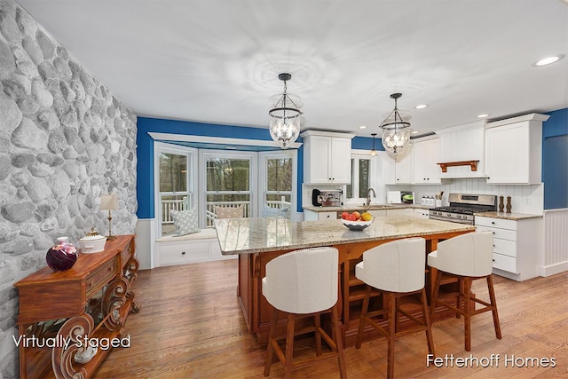 kitchen featuring light wood-type flooring, a notable chandelier, a kitchen island, and stainless steel gas range oven